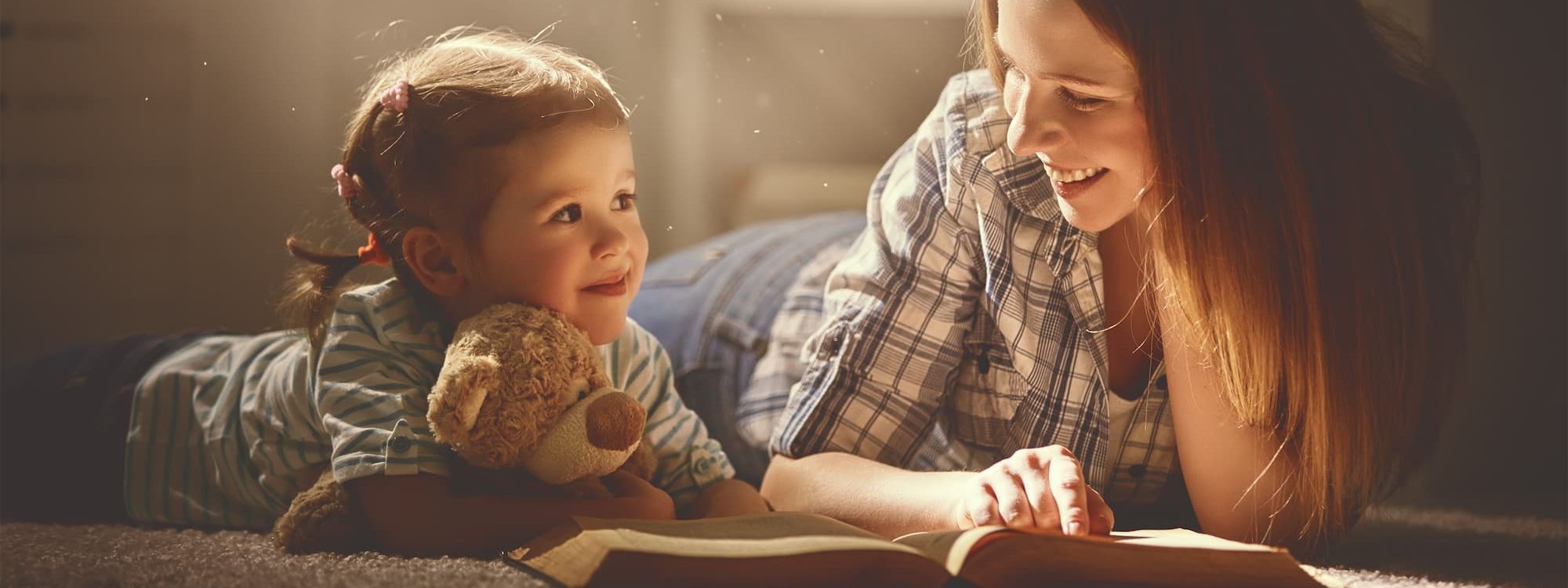Child reading book with woman and teddy bear